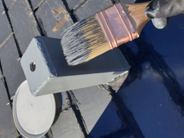 Adam tahta çatıda metal bir direği griye boyuyor