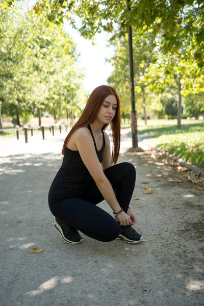 Young modern woman tying running shoes in urban park.stock photo