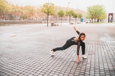 Spor giyim ve spor ayakkabı giymiş genç bir sporcunun kollarını uzatıp kameraya baktığı tüm vücut manzarası.