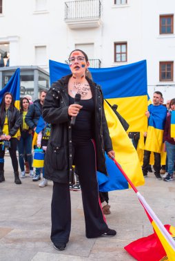 Estepona, Endülüs, İspanya - Mart. 05, 2022. Protestocular Ukrayna 'yı desteklemek için toplandılar. Yüzünde Ukraynalı, İspanyol ve Rus bayrakları olan kadın bir konuşma yapıyor..