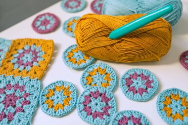 Pamuk topuna takılmış tığ işi kanca kapağı çok renkli örgü işi beyaz masa arasına yerleştirilmiş. Pamuk ipliğiyle örgü örmek.