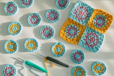 Çok renkli tığ işi motifleri ve iki kancalı tığ işi başladı. Beyaz yüzeyde pürüzlü doku, sert ışıkta koyu gölgeler. Tığ işi kalıpları oluşturma kavramı.