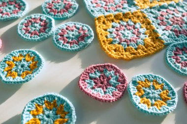 Beyaz yüzeyde yuvarlak ve kare şekilli dokulu tığ işi motiflerin yan görünüşü seçici odaklı, koyu gölgeli sert ışık. Çok renkli tığ işi desenleri kavramı.