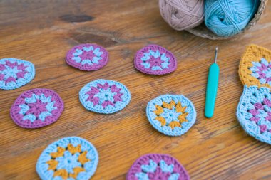 Tahta yüzeye odaklanmış küçük yuvarlak örgü desenleri, arkaplanda bulanık örgü kancası ve iplik izleri var. Tığ işi çok renkli desenler kavramı.