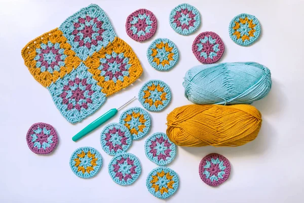 Flat lay of crochet patterns, hook and skeins of thread on white background. Concept of crocheting round and square motifs.