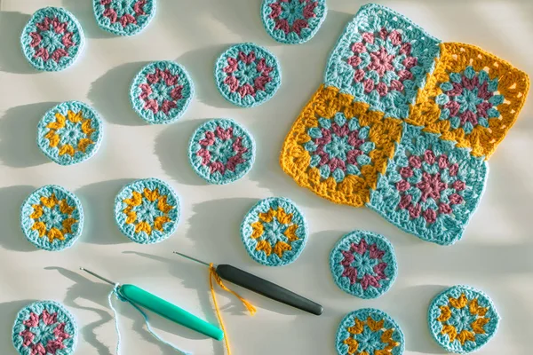 Çok renkli tığ işi motifleri ve iki kancalı tığ işi başladı. Beyaz yüzeyde pürüzlü doku, sert ışıkta koyu gölgeler. Tığ işi kalıpları oluşturma kavramı.