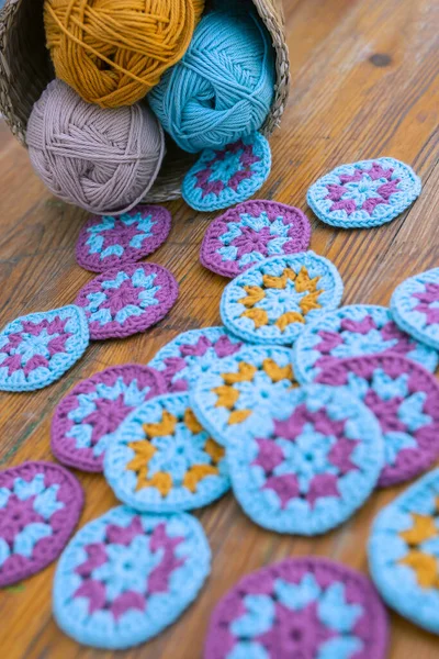 Multicolored crochet patterns overstrew on the wooden table and a small basket with cotton skeins in the corner. Concept of  materials for crocheting and knitting.