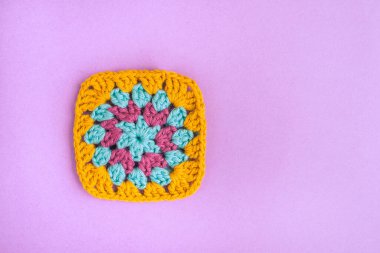 Closeup of multicolored bright crochet motif of square shape on light violet background. Beautiful and colorful crochet piece.