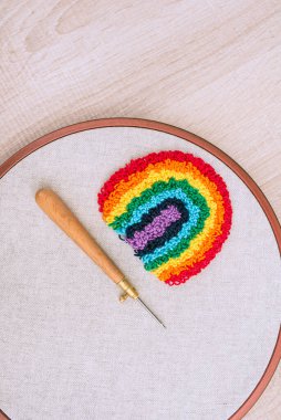 Büyük bir gökkuşağı desenli nakışlı çemberin üst görüntüsü, beyaz ahşap yüzeyde yumruk iğnesi ve iğne tekniğiyle yapılmış. İplik sanatı.