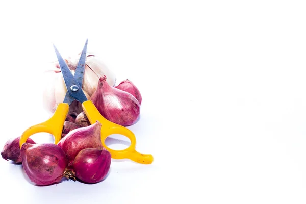 İzole edilmiş beyaz arka planda sarımsak ve soğan yığını arasında sarı makas. Güney Kalimantan, Endonezya. 12 Aralık 2021. 