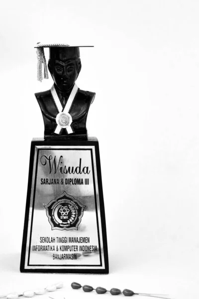 Mezuniyet gününde toga şapka takan bir heykelin silüeti. İzole edilmiş beyaz bir arka planı var. Siyah beyaz fotoğrafçılık. Güney Kalimantan, Endonezya. 23 Kasım 2014.