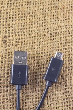 İzole edilmiş çuval bezi arkaplanındaki siyah mikro USB kablosunun iki ucu. Estetik fotoğrafçılık. Ürünler, cep telefonu aksesuarları, güç, teknoloji ve bağlantılar için kopyalama alanı.
