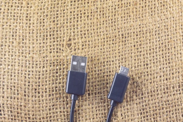 İzole edilmiş bir çuval bezi arka planında mikro usb ve usb siyah mikro usb kablo. Estetik fotoğrafçılık. Ürünler, cep telefonu aksesuarları, güç, teknoloji ve bağlantılar için kopyalama alanı.