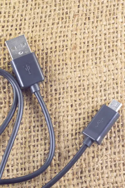 Akıllı telefondan bilgisayara veri kopyalamak için veri kablosu ve izole edilmiş bir çuval bezi arka planında da tam tersi. Estetik fotoğrafçılık. Ürünler, cep telefonu aksesuarları, teknoloji ve bağlantılar için kopyalama alanı.
