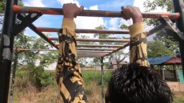 Bir adam barfiks tarzıyla fitness yapıyor. Demir çubuğu yukarı ve aşağı hareket halinde omuz genişliğinde tutun. Arka tarafta üst konum ve tutuş. Güney Kalimantan, Endonezya. 16 Temmuz 2022.