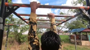 Bir adam barfiks tarzıyla fitness yapıyor. Demir çubuğu yukarı ve aşağı hareket halinde omuz genişliğinde tutun. Arka tarafta üst konum ve tutuş. Güney Kalimantan, Endonezya. 16 Temmuz 2022.