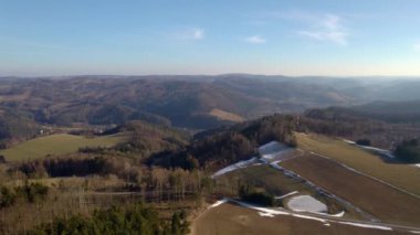 Tepeleri ve tepeleri olan güzel bir manzara ağaçlar ve ormanlarla kaplı güneşli bir günde karla kaplı tarlalar ve mavi ufuk manzaralı.