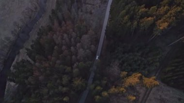 Ağaçlarla dolu bir arazide gün batımında küçük bir köye gelen bir araba.