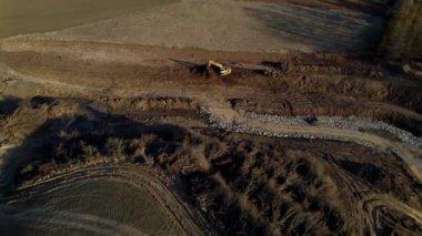 Yellow excavator standing on the construction of a new road in the middle of the fields at sunset