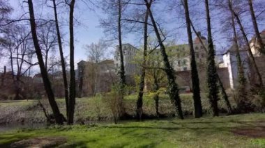 Nehir ve ağaçlarla dolu Olomouc şehir parkı, bir bahar sabahı şehrin duvarları ve tarihi binalar manzarası