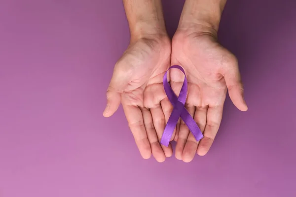 Purple ribbon as symbol of World Cancer Day over purple color background, copy space.