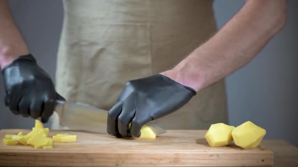 Close-up of mens hands in black disposable gloves. The cook in an apron s slicing potatoes on a cutting board. — Stock Video