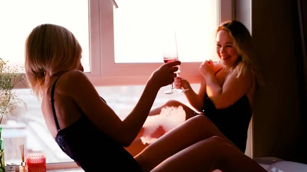 Φιλενάδες με εσώρουχα πίνουν σαμπάνια ενώ κάθονται κοντά σε ένα μπάνιο με αφρό και ροδοπέταλα — Φωτογραφία Αρχείου