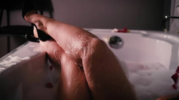 Gros plan d'une femme détendue se relaxant dans un bain moussant. Une femme touche sa peau avec une fleur d'hortensia bleue. — Photo