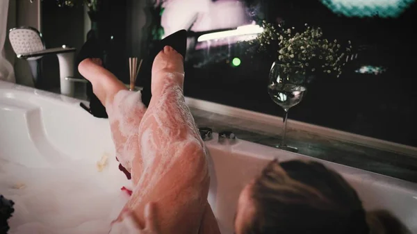 Close-up de uma mulher relaxada relaxante em um banho de espuma. Uma mulher toca sua pele com uma flor de hortênsia azul. — Fotografia de Stock