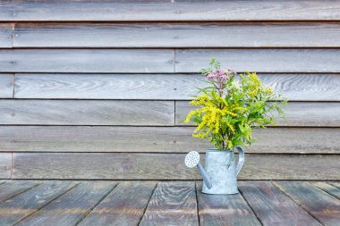 Ağaç bir duvarın önündeki tahta bir yüzey üzerindeki su kabındaki kır çiçekleri. Kopya uzay, yatay görüş 1