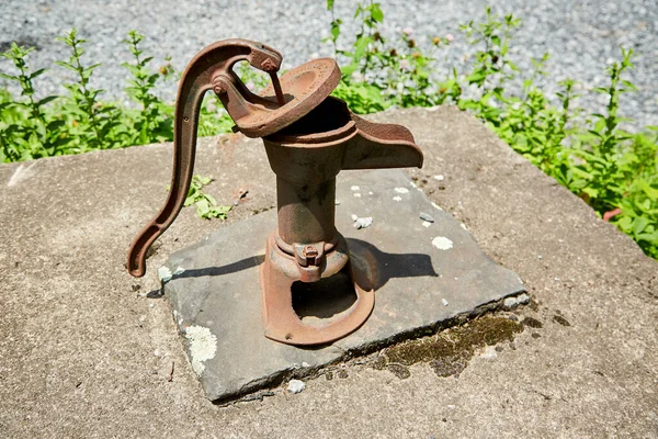 带苔藓的石井盖上的生锈手动水泵 — 图库照片