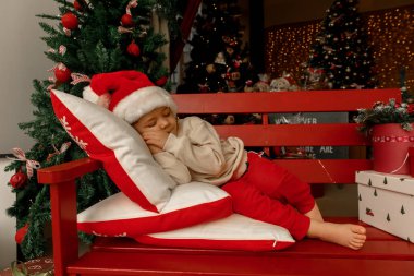 Noel Baba 'lı bir çocuk Noel ağacının yanında uyur ve gülümser.