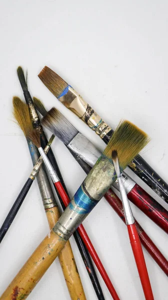 Bir grup tahta ve plastik sanatçının dikey çekimleri farklı şekil ve boyutlarda fırçalar ve beyaz arka planda birbirlerinin üzerinde renk lekeleri bulunur.