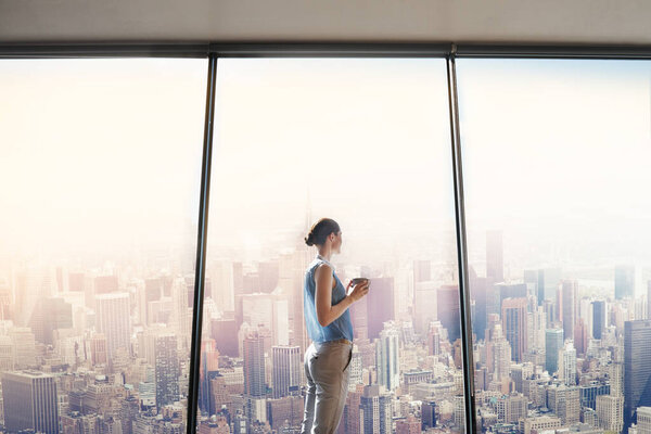 Shot of an attractive young woman looking out from a large window in the office