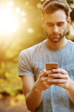 Parkta cep telefonuyla mesajlaşan genç bir adamın görüntüsü.