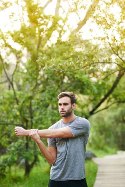 Parkta koşuya çıkmadan önce esneme hareketleri yapan genç bir adam.
