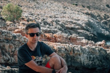 Bir adam oturur ve dizini kayalık dağların arka planına yaslar.