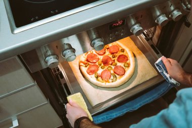 Erkeğin ellerinin fırından ev yapımı pizzayı çıkarmasını daha da büyütüyor..