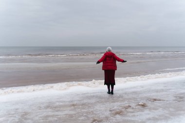 Denize bakan bir kadın kollarını yanlara açmış, arkadan manzarayı seyrediyor..