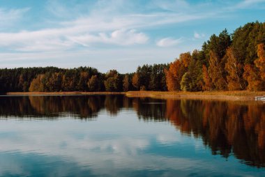 Litvanya 'nın Labanoras Bölgesel Parkı' ndaki Baltieji Lakajai Gölü 'nün sularına çok renkli ve bulutlu bir sonbahar ormanı ve gökyüzü yansımaktadır..