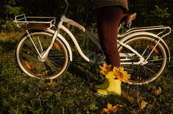 Rower z koszykiem w jesiennym lesie z kobietą stojącą w żółtych gumowych butach, wypełniony żółtymi liśćmi. — Zdjęcie stockowe