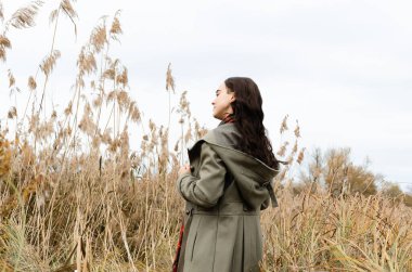 Genç, hayalperest, düşünceli, esmer, gri, eski moda palto giyen kadın kuru çim kamışları tarlasında dikiliyor, başka tarafa bakıyor.. 