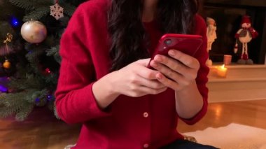 Tanınmayan bir kadının elinde, akıllı telefonunu Noel sezonunda kaydırıyor. İnternet üzerinden alışveriş, sosyal medya.