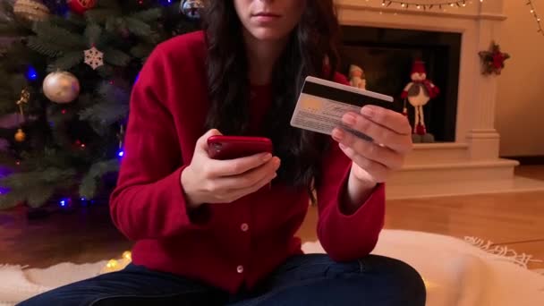 Невпізнавана жінка, яка купує на Різдво подарунки онлайн на своєму смартфоні, тримає кредитну картку. — стокове відео
