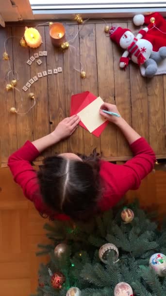 Ovanifrån av kvinna underteckna semester julkort, sätta den i rött kuvert, sitter bredvid julen dekorerad träd. — Stockvideo