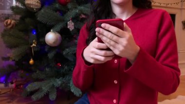 Tanınmayan bir kadının elinde, akıllı telefonunu Noel sezonunda kaydırıyor. İnternet üzerinden alışveriş, sosyal medya.