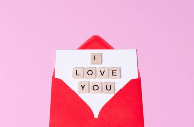 Red envelope with wooden words I love you on a pink pastel copy space background. St Valentines Day letter concept. 