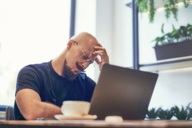 Mutsuz adam el ele tutuşuyor. Yorgun işadamı iş yerinde dizüstü bilgisayarla oturuyor. Baş ağrısı hissediyor.