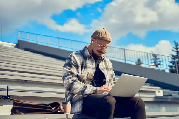 Концентрований бородатий чоловік сидить на відкритому повітрі і друкує текст на ноутбуці. Підключення до Інтернету 4G — стокове фото