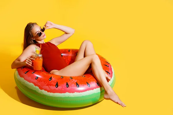 Full length slim girl wears red swimsuit sits on inflatable ring isolated on yellow background — Stock Photo, Image